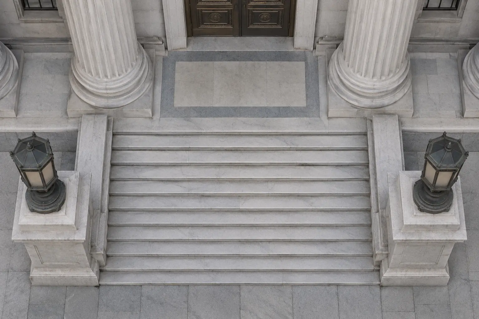 Stone steps rising to the columned entrance of a government building, with a lantern on each side and a doorway at the top.